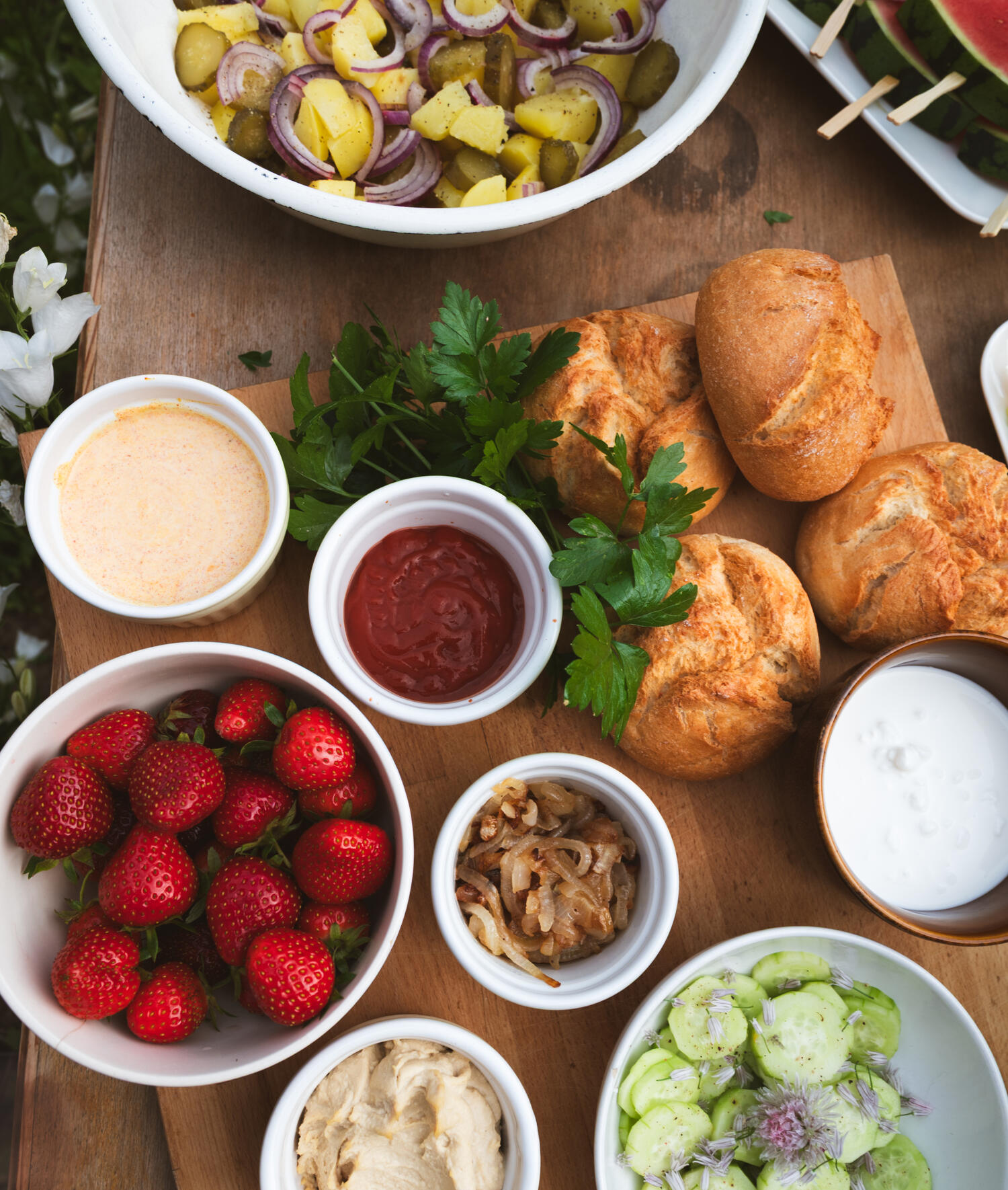 Stół grillowy z dodatkami: pieczywo, sałatka ziemniaczana, cebulka, sosy, sałatka ogórkowa